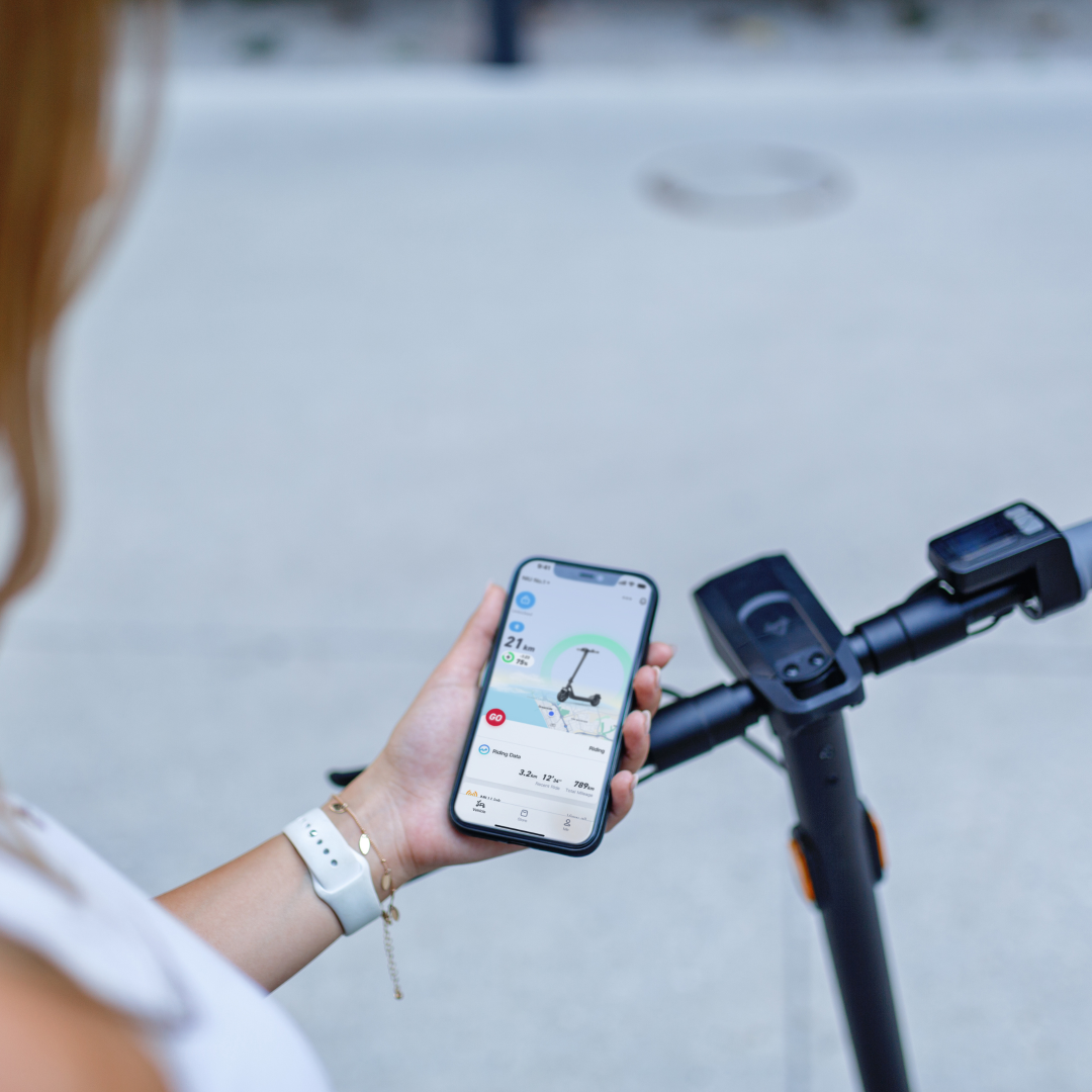 NIU - KQi100F Electric KickScooter lifestyle photo with consumer using NIU app for kickscooter